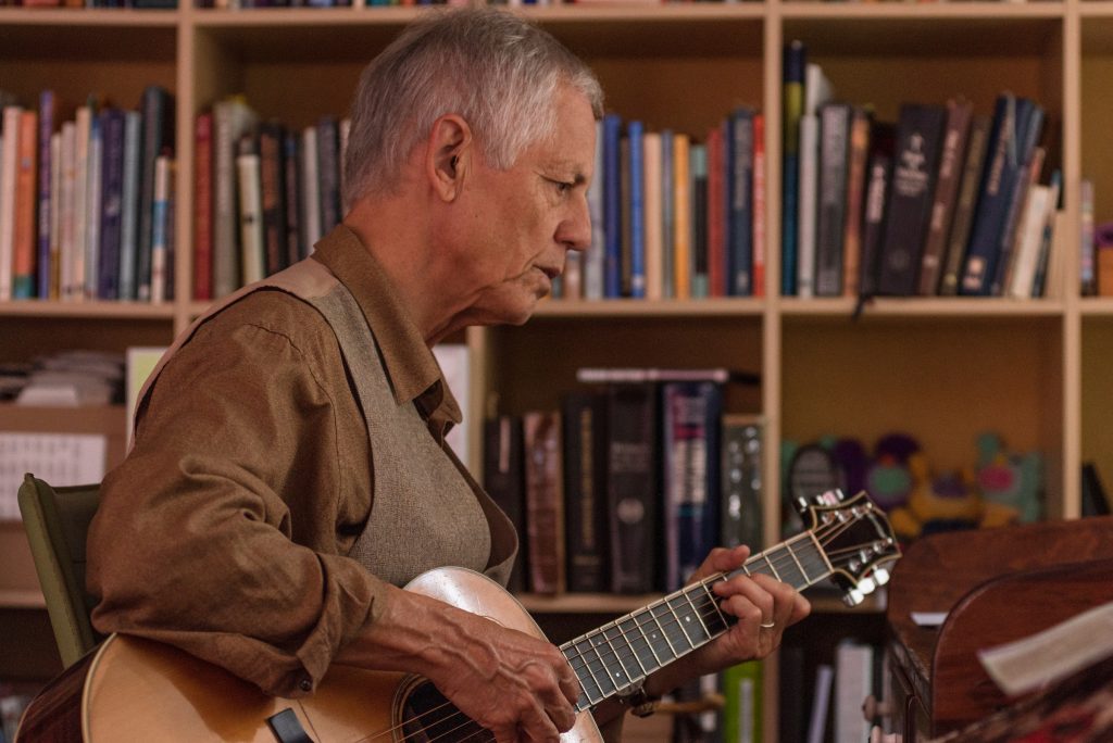 Rudi Harst playing guitar in front of bookshelves