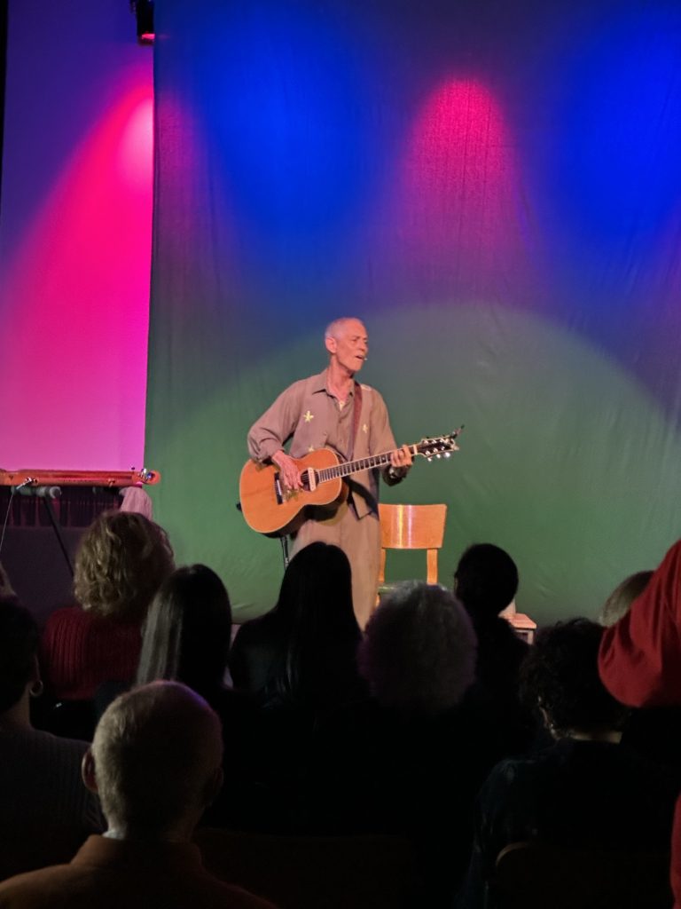 Rudi Harst playing guitar onstage under colorful lights