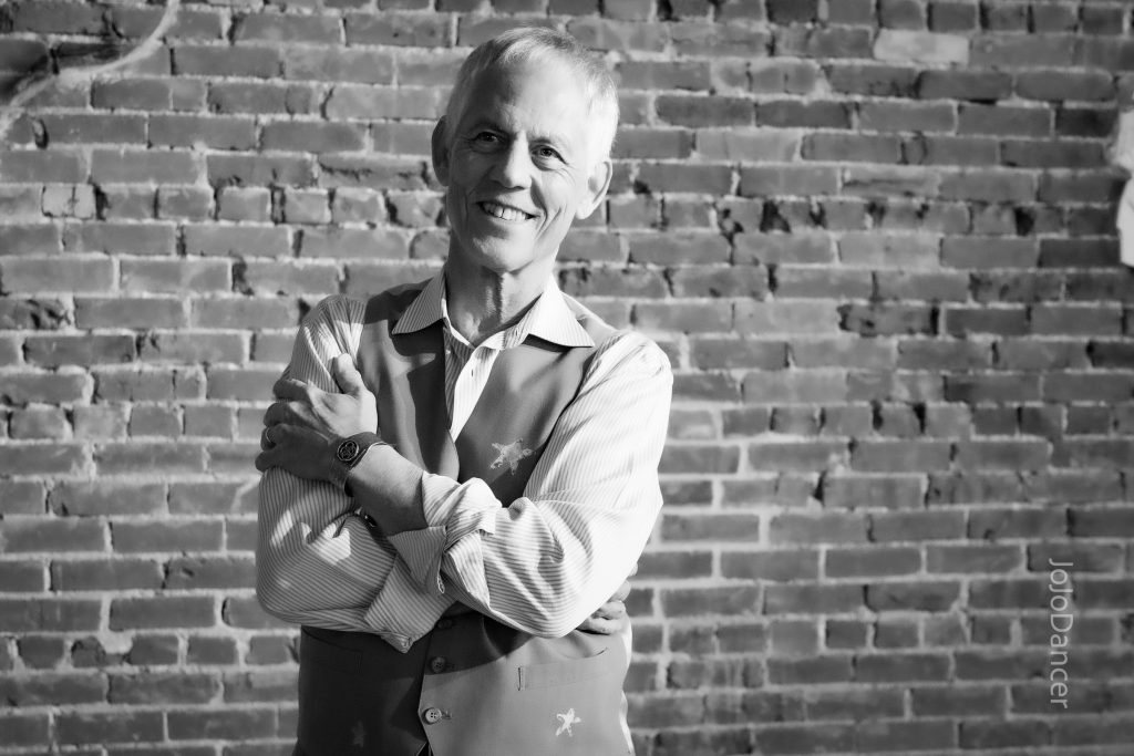 Rudi Harst smiling in a brick-walled studio
