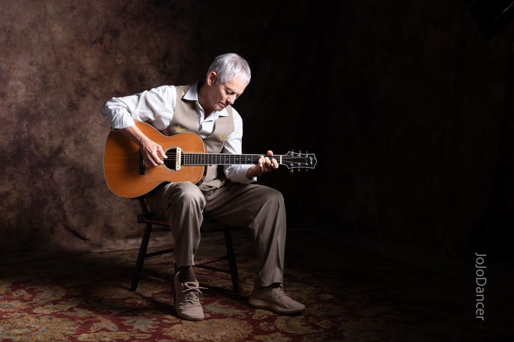 Rudi Harst seated with his acoustic guitar
