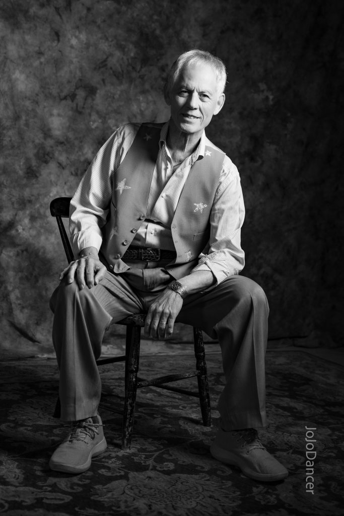 Black-and-white seated portrait of Rudi Harst with guitar