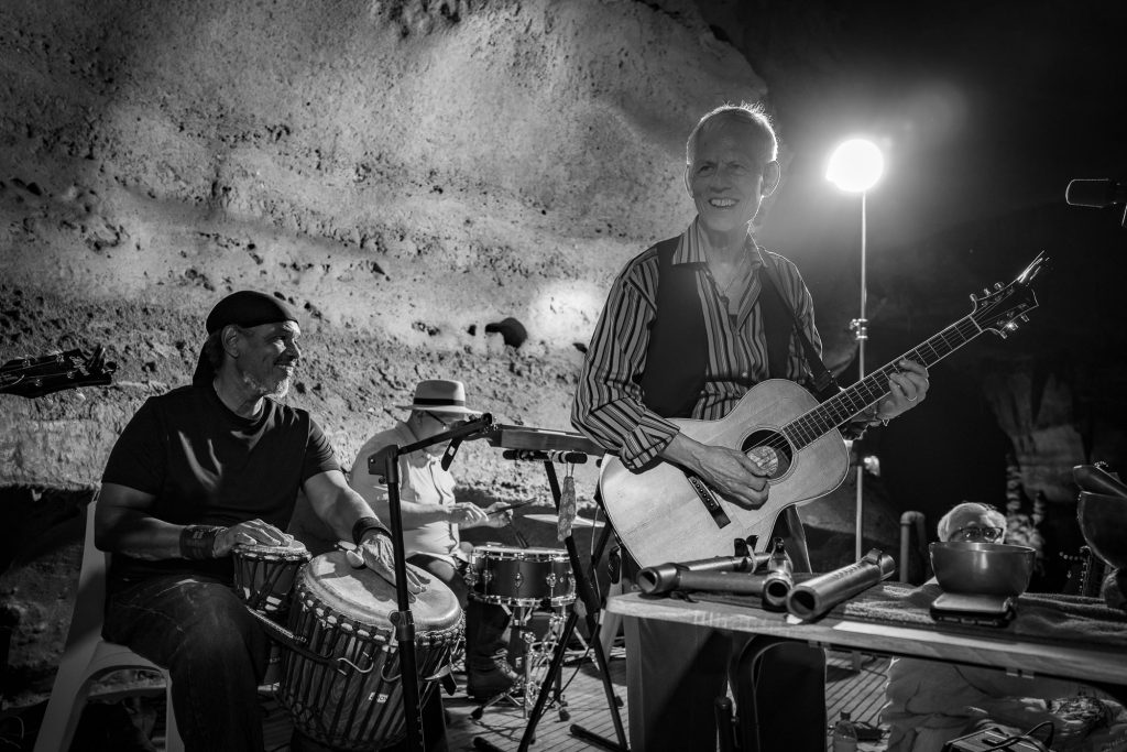 Monochrome view of Rudi Harst with guitar beside a hand drummer and bright stage light
