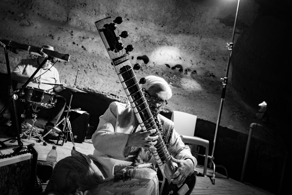 Monochrome view of a seated sitar player with a drummer behind him