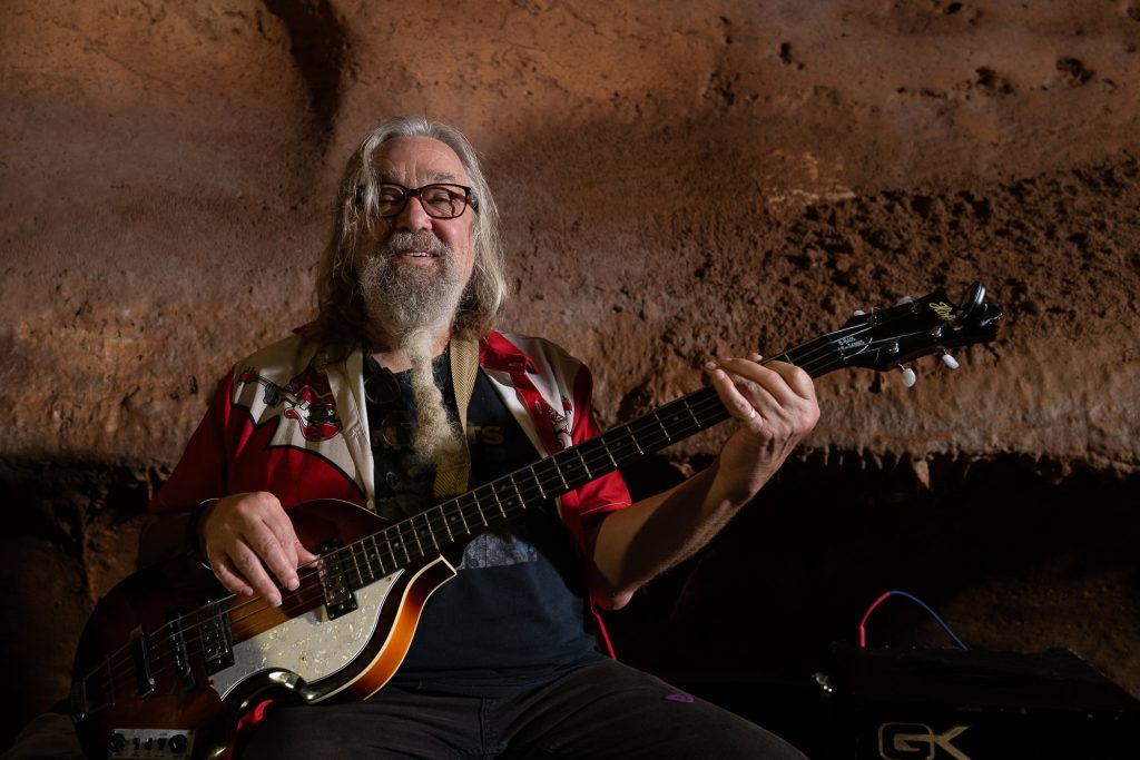 A smiling bassist seated against the cave wall