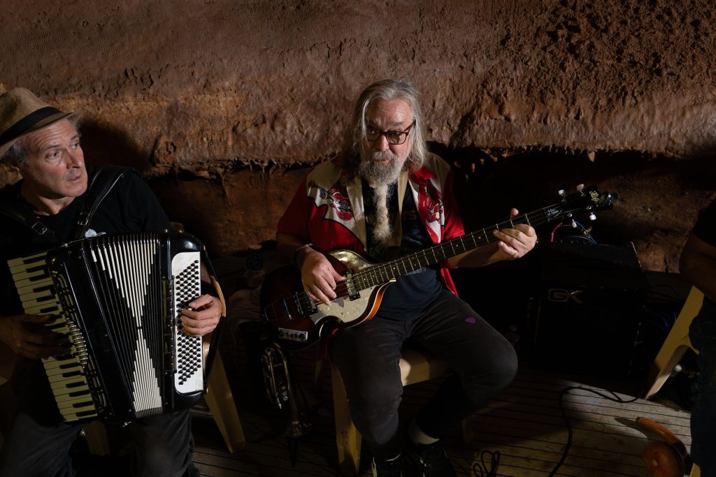 An accordionist and bassist seated together against the cave wall