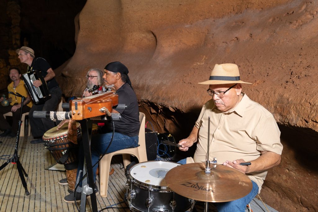 A drummer in a light hat performing with the ensemble behind him