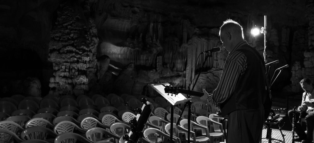Monochrome side view of Rudi Harst at a keyboard facing rows of empty chairs