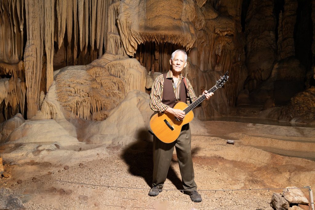 Wide portrait of Rudi Harst facing the camera with his acoustic guitar