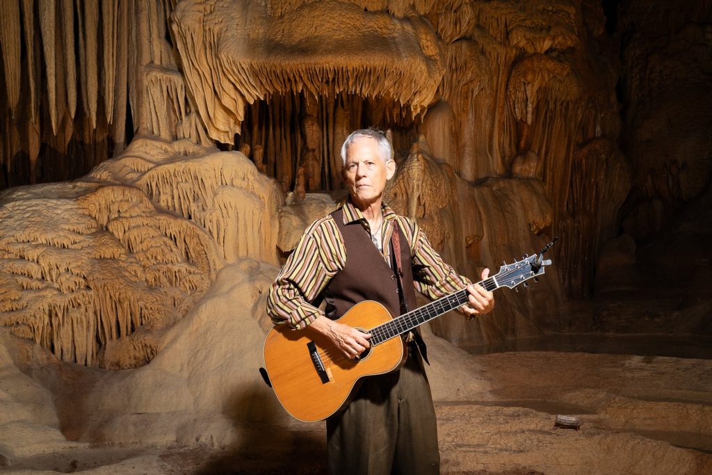 Closer portrait of Rudi Harst holding a guitar across his waist