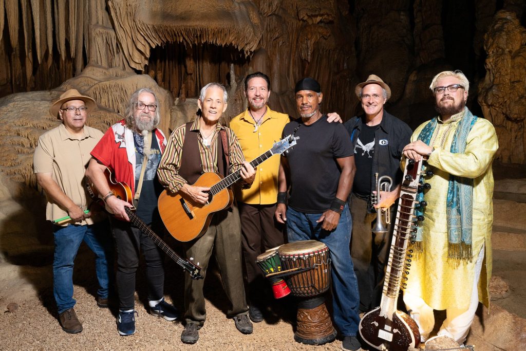 Rudi Harst and six fellow musicians standing together with guitar, drums and sitar