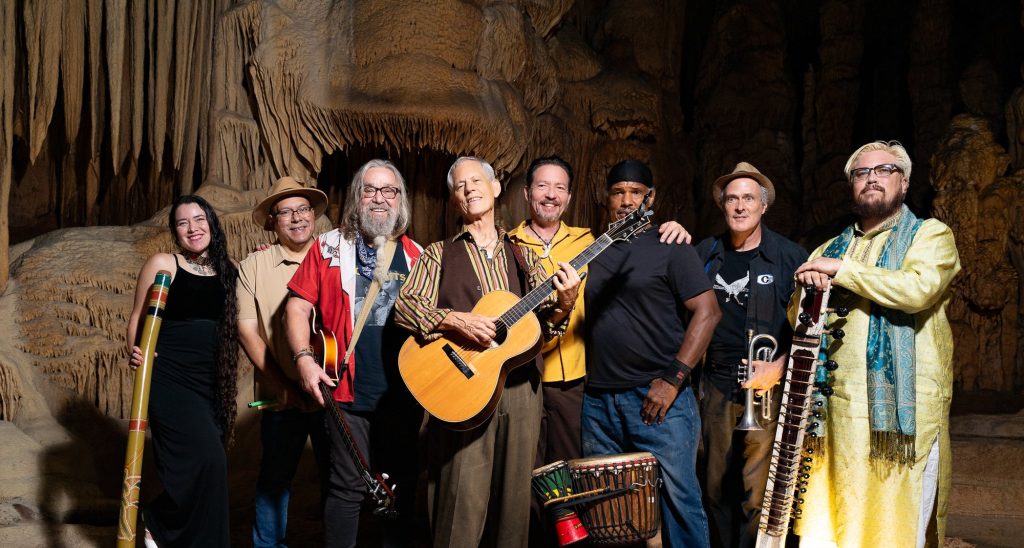 Rudi Harst and seven fellow musicians smiling beneath cave formations