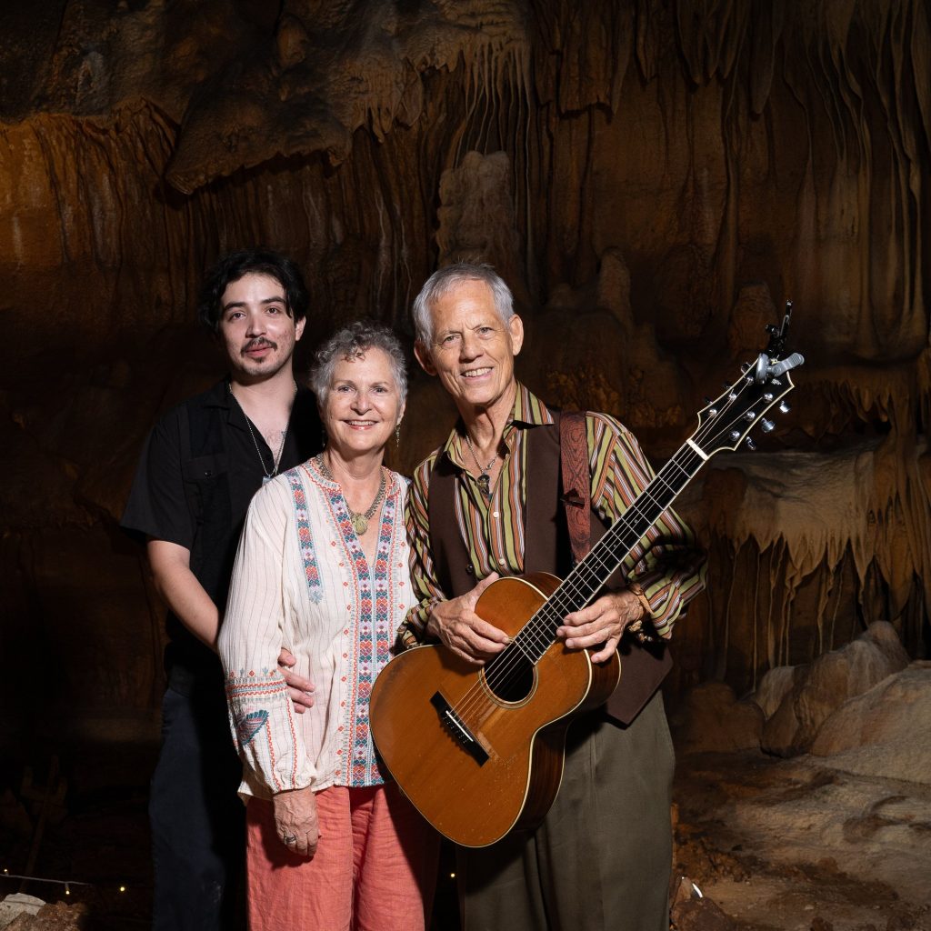 Vertical portrait of Rudi Harst and two visitors with his acoustic guitar