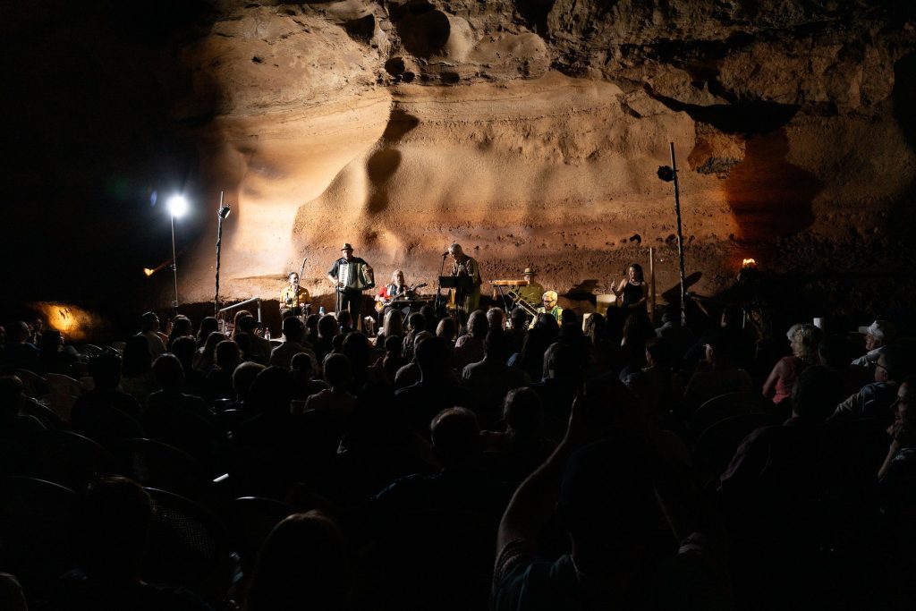 The audience watching the ensemble under the broad cave ceiling