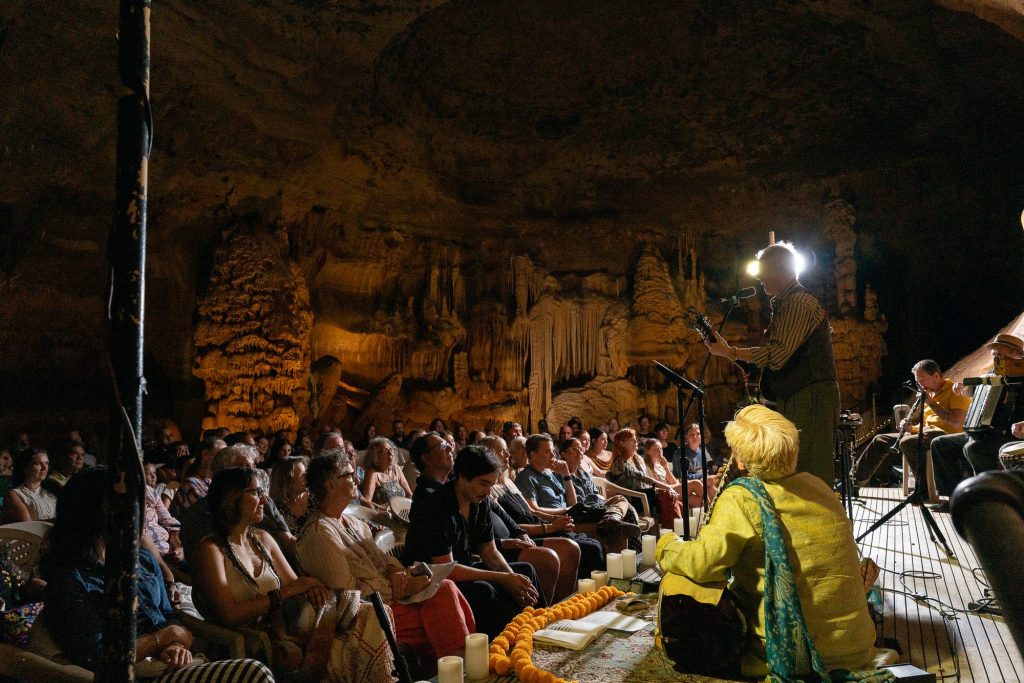 Rudi Harst playing toward the audience beneath warm cave lighting