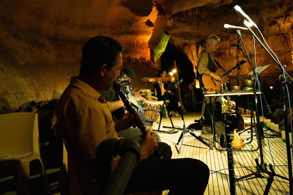 A seated wind player in a yellow shirt with Rudi Harst performing behind him