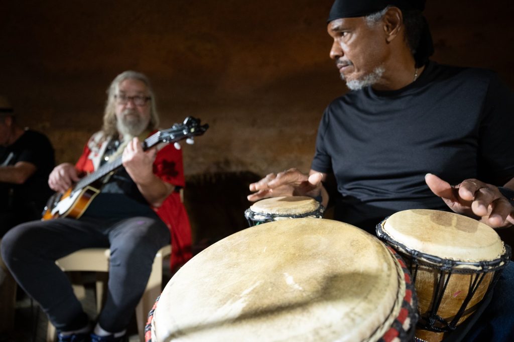 Close view of a percussionist playing two hand drums with a bassist behind him