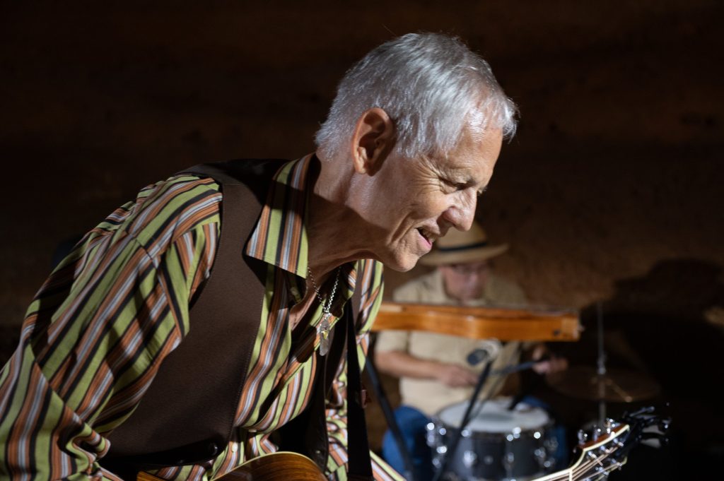 Rudi Harst leaning forward and smiling beside the drum kit