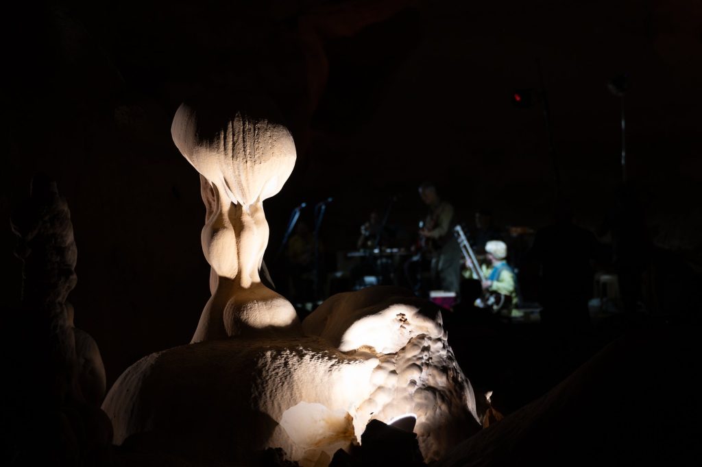 An illuminated cave formation with the ensemble visible in the distance