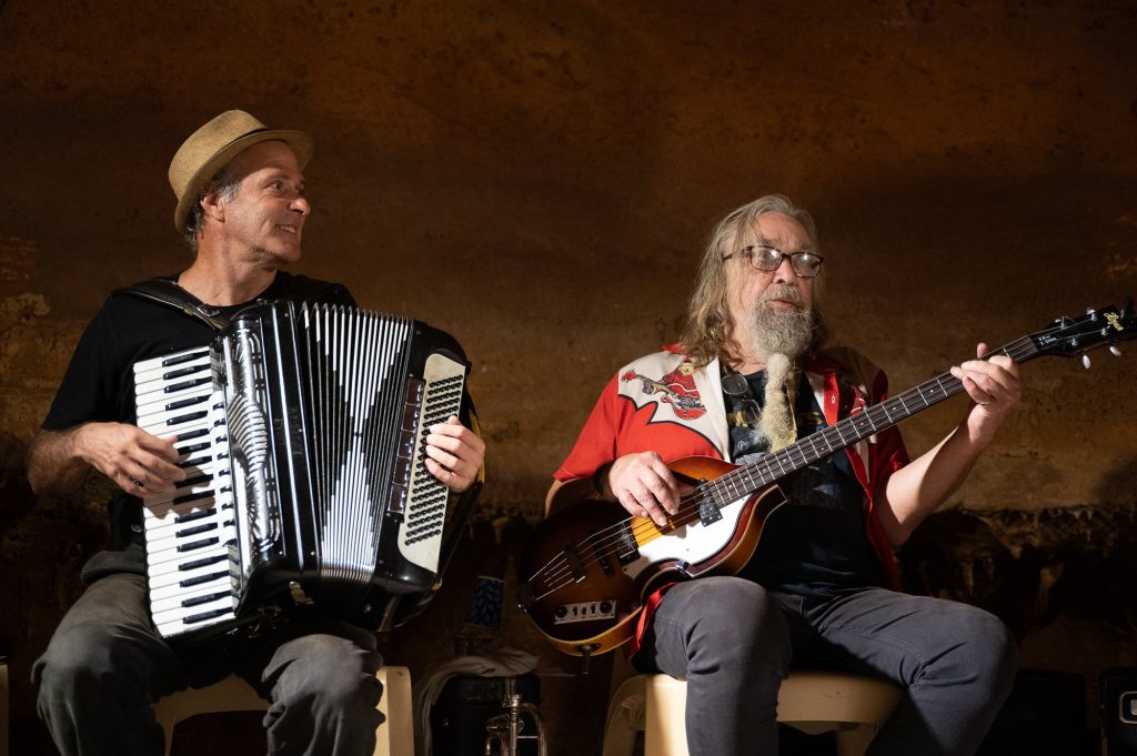 An accordionist and bassist performing together against the cave wall
