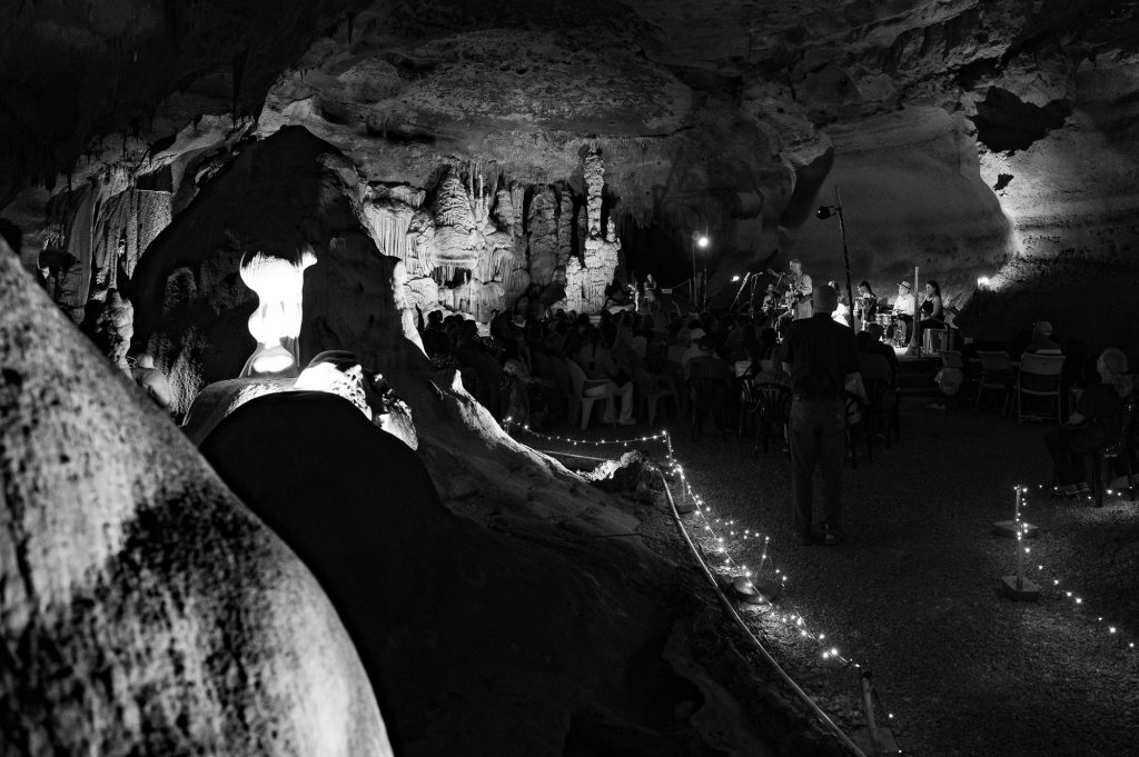 Monochrome view along a light lined cave walkway toward the concert