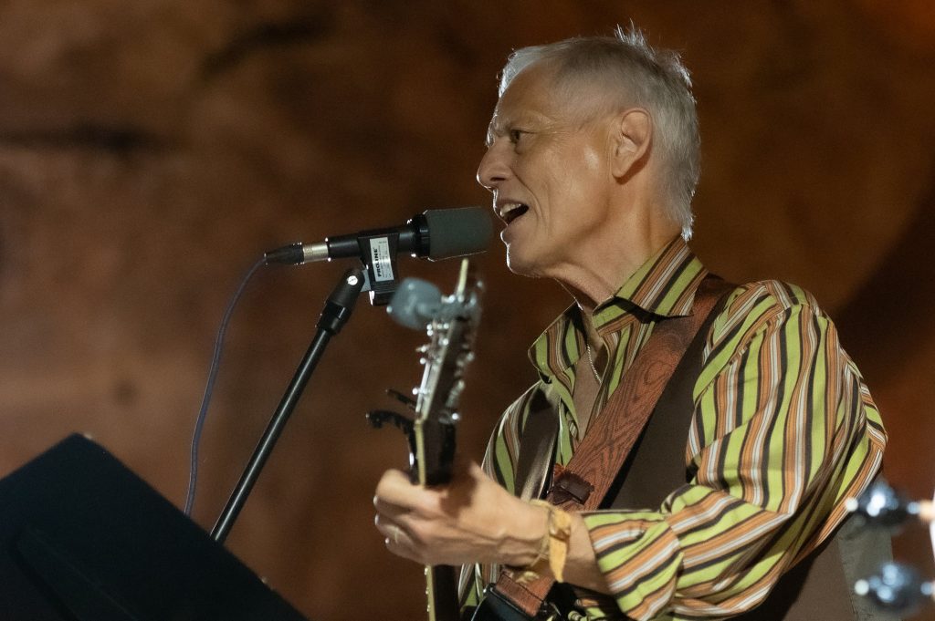Close profile of Rudi Harst singing into a microphone while playing guitar