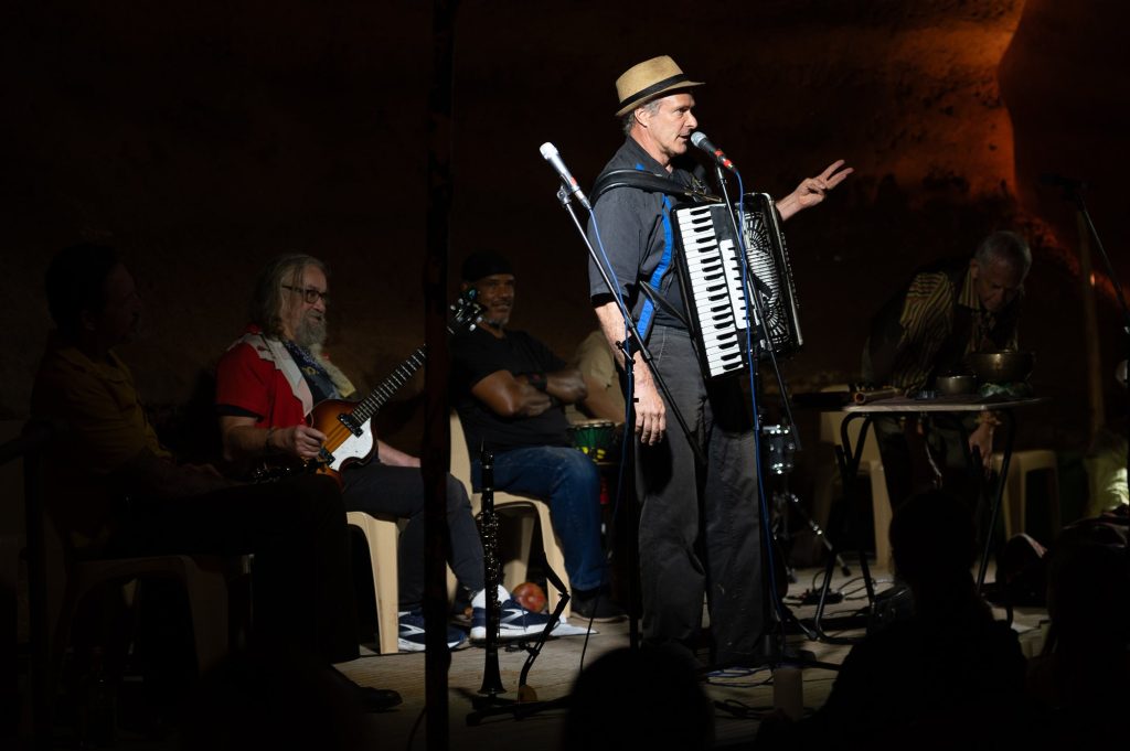 A standing accordionist gesturing toward the audience with musicians behind him