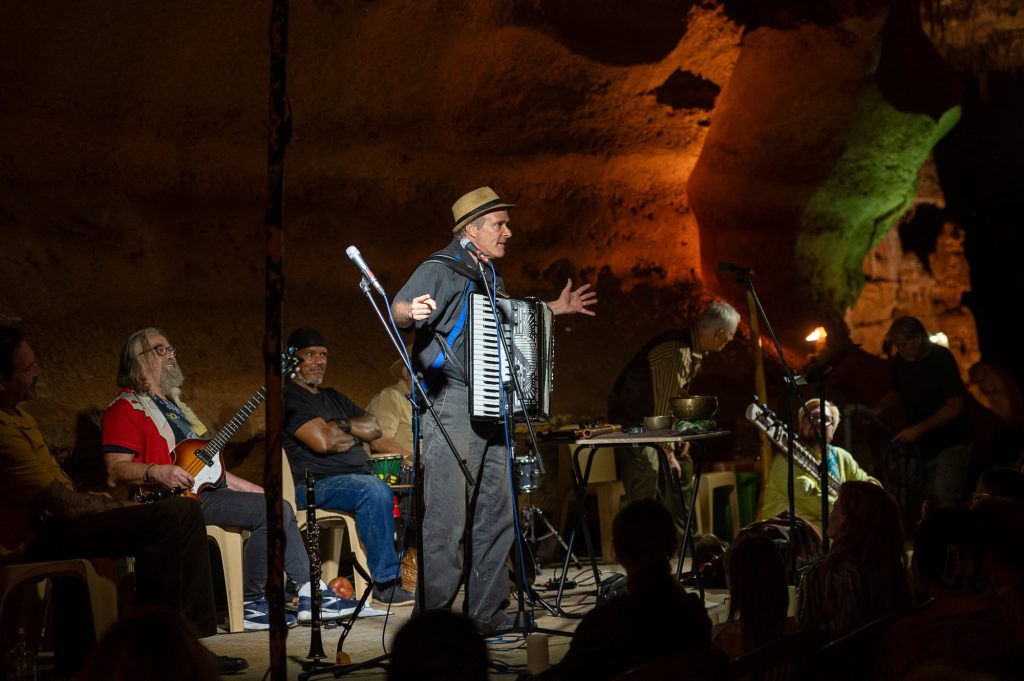 Wide view of an accordionist addressing the audience from the cave stage